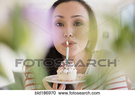 Stock Image - Woman blowing out birthday candle on cupcake. Fotosearch