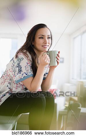 Stock Photograph - Woman drinking cup of coffee in living room. Fotosearch