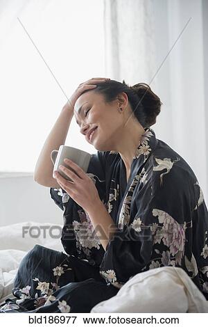 Woman drinking cup of coffee on bed View Large Photo Image Stock Photo - Woman drinking cup of coffee on bed. Fotosearch