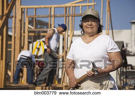 Stock Photo - Woman holding hammer at construction site. Fotosearch