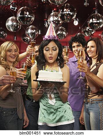 Stock Image - Woman in party hat blowing out candles on birthday cake. Fotosearch