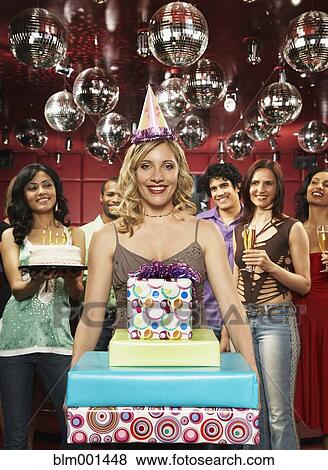Stock Photo - Woman in party hat holding stack of birthday presents. Fotosearch