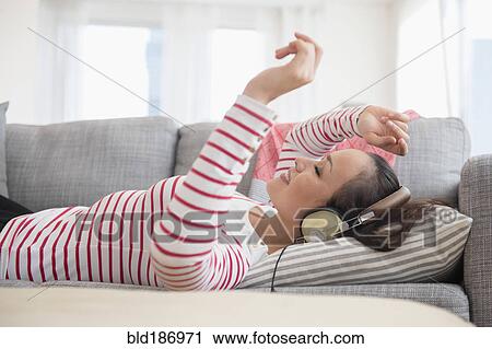 Stock Image - Woman listening to headphones on sofa. Fotosearch