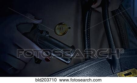 Stock Image - Woman putting pistol in purse. Fotosearch