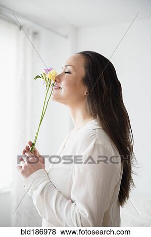 Stock Photo - Woman smelling flowers indoors. Fotosearch