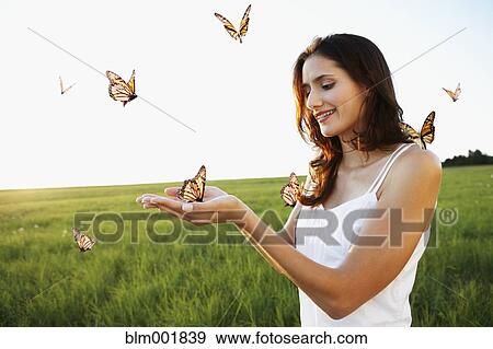 Stock Photo - Woman standing among butterflies in meadow. Fotosearch