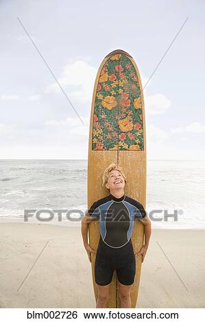 Stock Photograph - Woman standing in front of surfboard at beach. Fotosearch