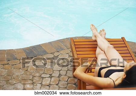 Picture - Woman sunbathing next to swimming pool. Fotosearch