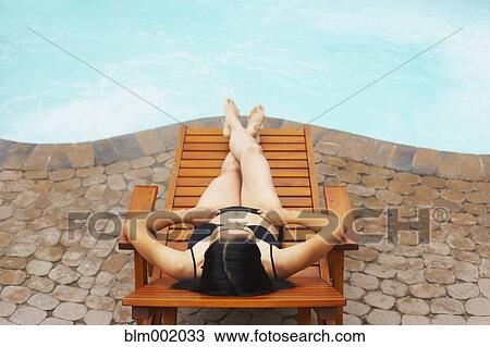 Stock Image - Woman sunbathing next to swimming pool. Fotosearch