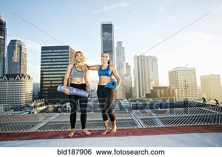 Women holding yoga mats on urban rooftop View Large Photo Image Stock Photograph - Women holding yoga mats on urban rooftop. Fotosearch
