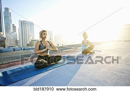 Stock Image - Women practicing meditating on urban rooftop. Fotosearch