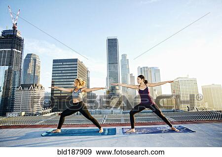 Stock Photo - Women practicing yoga on urban rooftop. Fotosearch