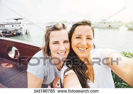 Stock Photography - Women taking selfie on Ha Long Bay waterfront, Vietnam. Fotosearch