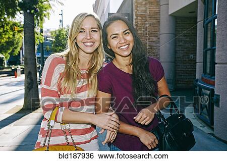 Stock Photograph - Women walking arm-in-arm on sidewalk. Fotosearch