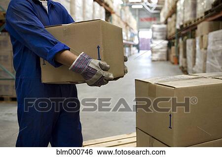 Stock Photograph - Worker carrying boxes in warehouse. Fotosearch