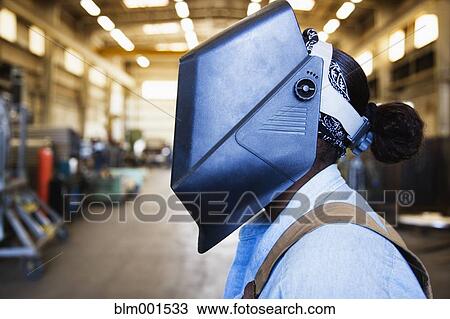 Stock Image - Worker wearing welding mask in warehouse. Fotosearch