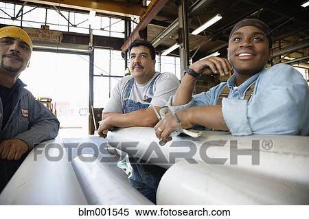 Stock Photography - Workers leaning on metal pipes in warehouse. Fotosearch