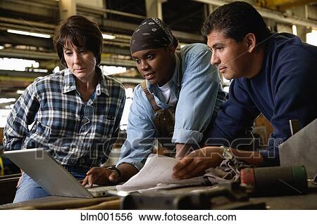 Stock Photograph - Workers looking at laptop in warehouse. Fotosearch