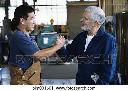 Stock Image - Workers shaking hands in warehouse. Fotosearch