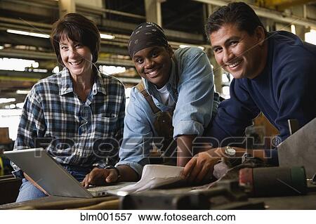 Stock Photo - Workers smiling with laptop in warehouse. Fotosearch