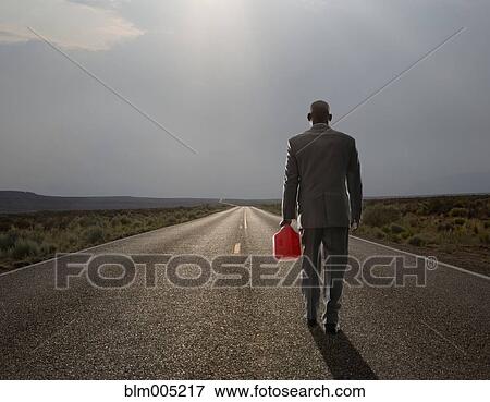 Stock Photo - African American businessman carrying gas can on remote highway. Fotosearch