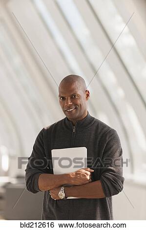 Stock Photograph - African American businessman carrying papers in lobby. Fotosearch