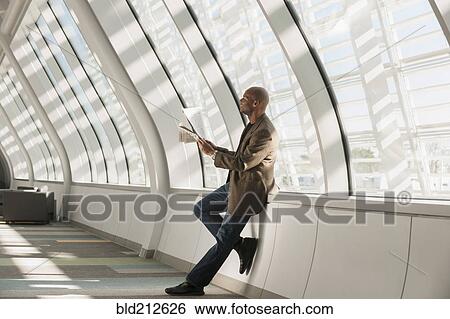 Stock Photograph - African American businessman reading newspaper in lobby. Fotosearch