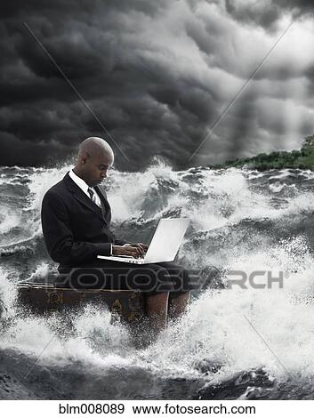 Stock Photo - African American businessman using laptop in stormy sea. Fotosearch