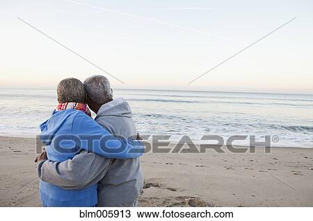 Stock Image - African American couple hugging on beach. Fotosearch