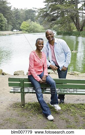 Stock Photo - African American couple sitting on bench near lake. Fotosearch