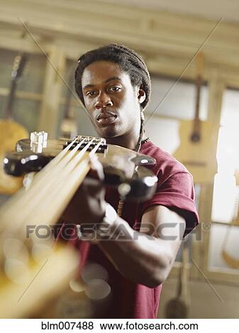 Stock Photo - African American craftsman looking at guitar in workshop. Fotosearch