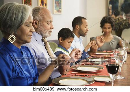 Stock Photo - African American family saying grace at dining table. Fotosearch
