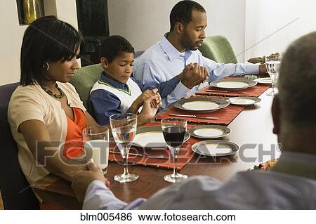 Stock Photograph - African American family saying grace at dining table. Fotosearch
