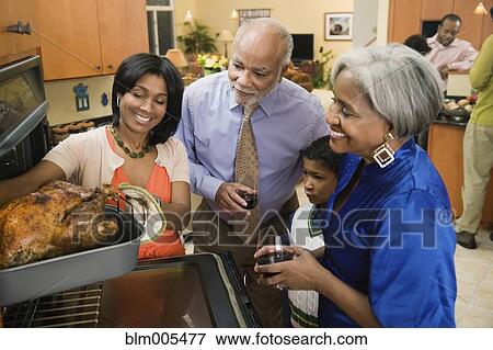 African American Family Watching Woman Take Thanksgiving Turkey From Oven Stock Photo Blm005477 Fotosearch