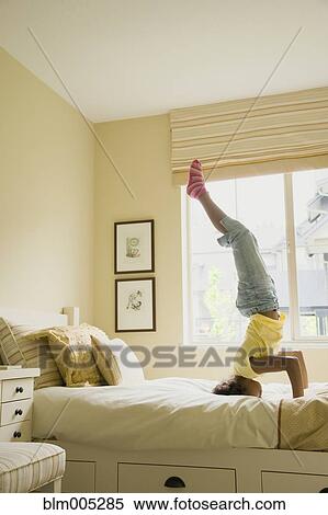 Stock Photography - African American girl doing headstand on bed. Fotosearch
