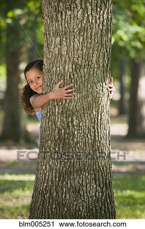 Stock Image - African American girl hugging tree trunk. Fotosearch