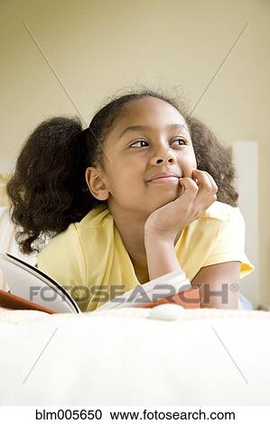 Stock Image - African American girl reading book in bed. Fotosearch