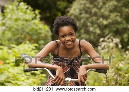 Stock Image - African American girl sitting on bicycle in backyard. Fotosearch