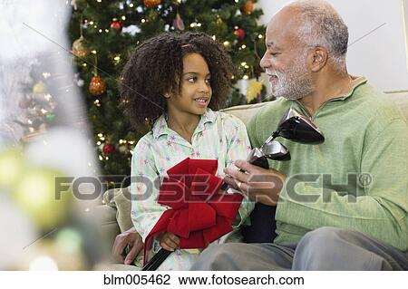 Stock Image - African American granddaughter giving grandfather Christmas gift. Fotosearch