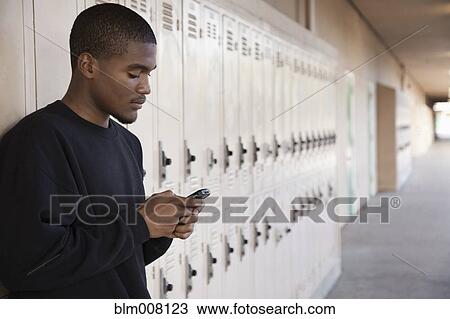 Stock Image - African American high school student using cell phone near lockers. Fotosearch