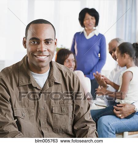 Stock Image - African American man in living room with family. Fotosearch