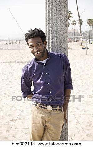 Picture - African American man leaning on pole at beach. Fotosearch