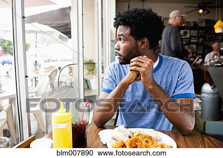 Stock Image - African American man looking out diner window. Fotosearch