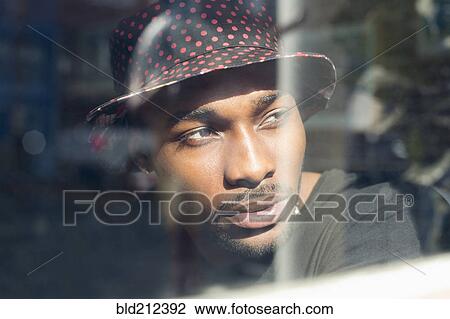 Stock Image - African American man looking out window. Fotosearch