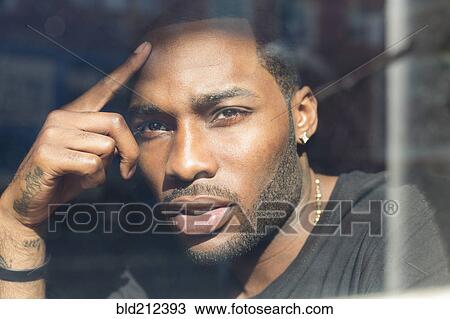 Stock Image - African American man looking out window. Fotosearch