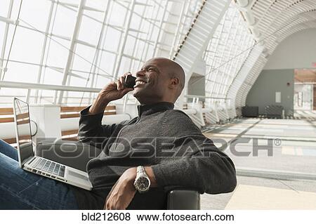 Stock Photo - African American man on cell phone in lobby. Fotosearch