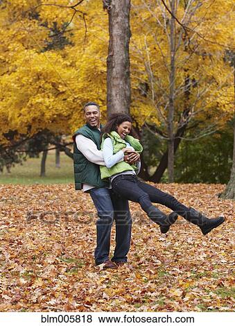 Stock Photo - African American man playing with wife in autumn leaves. Fotosearch