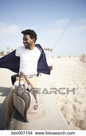 Picture - African American man removing shirt at beach. Fotosearch