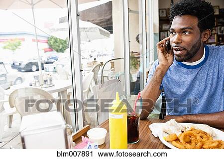 Stock Image - African American man talking on cell phone in diner. Fotosearch