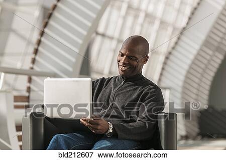 Stock Photo - African American man using laptop in lobby. Fotosearch